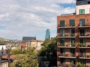 A multi-story building with balconies, a view of a distant modern skyscraper, and surrounding residential buildings. - Bright Stylish 2BR Escape in Charming Vera (T`bilisi)