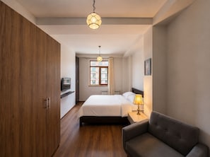 A modern hotel room with a bed, bedside table, lamp, and a view of the city through a window. - Bright Stylish 2BR Escape in Charming Vera (T`bilisi)