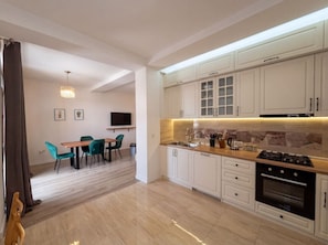 A modern kitchen with white cabinets, a dining area with a table and chairs, and a TV mounted on the wall. - Bright Stylish 2BR Escape in Charming Vera (T`bilisi)