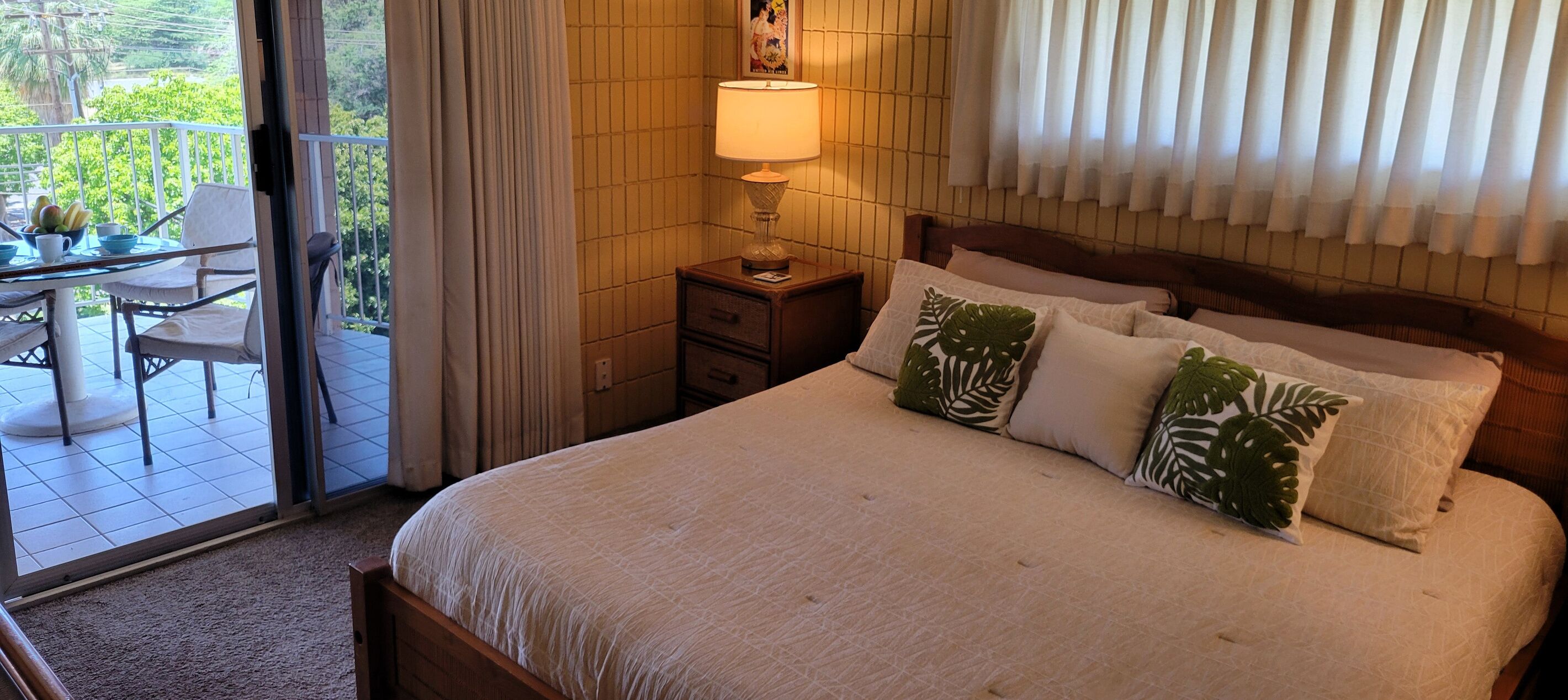 Une chambre à coucher comprenant un lit, une table de chevet, une lampe, une fenêtre avec des rideaux et un balcon avec une table et des chaises.