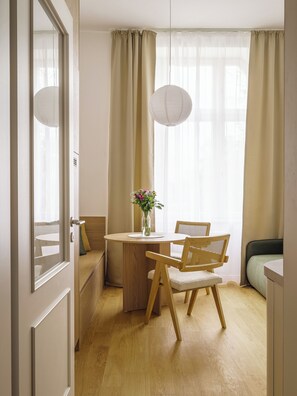 Ein Zimmer mit einem runden Holztisch, zwei Korbstühlen, einer Blumenvase und einem Bett mit grüner Bettdecke.