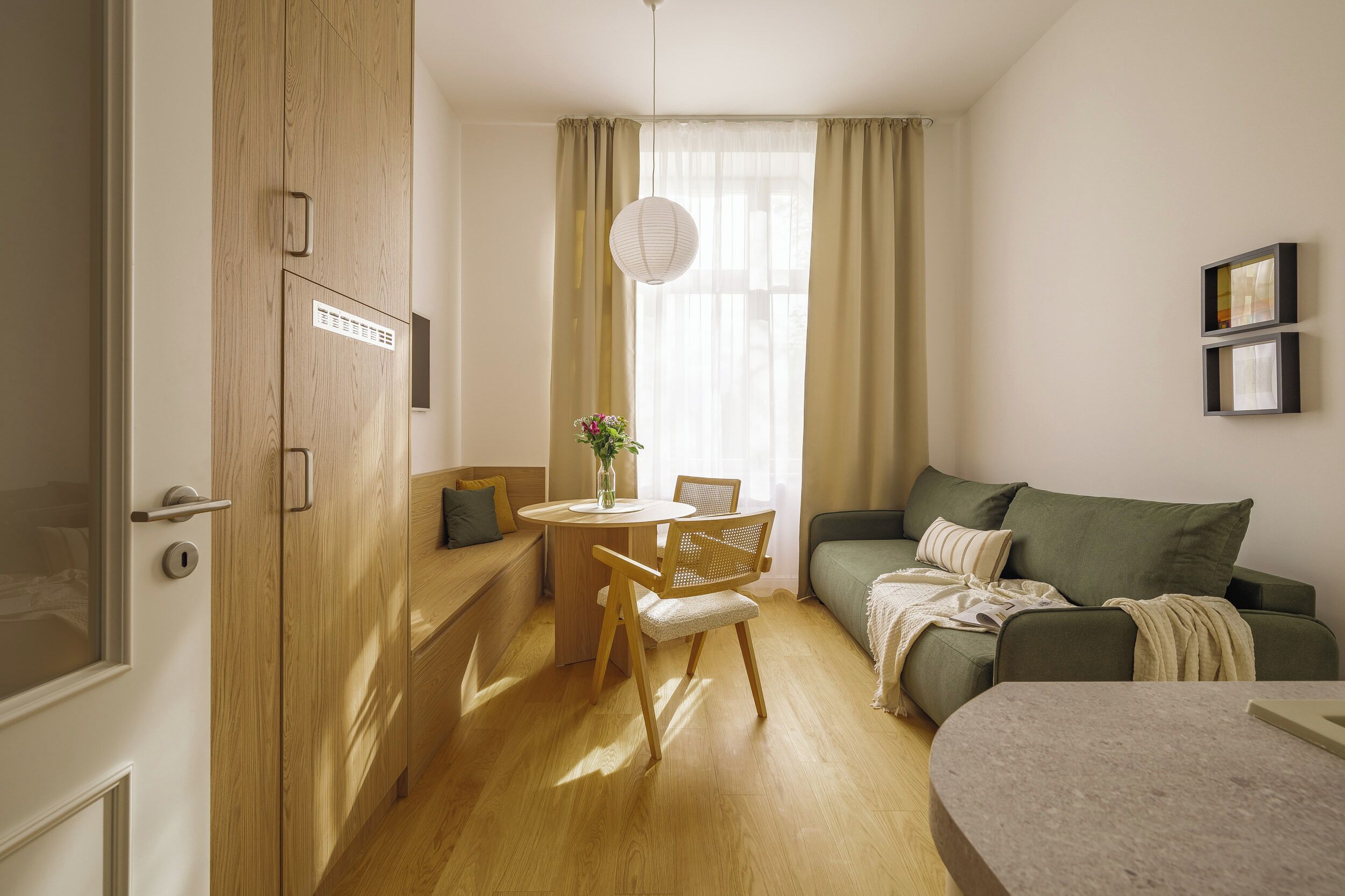 A compact living space with a wooden door, a round dining table with chairs, a sofa, and a small table with a vase.