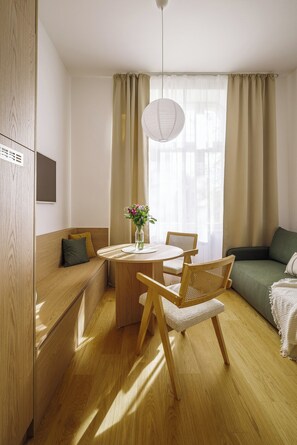 Ein gemütliches Zimmer mit einer hölzernen Bank, einem runden Tisch mit Stühlen, einer Pendelleuchte und einem grünen Sofa.