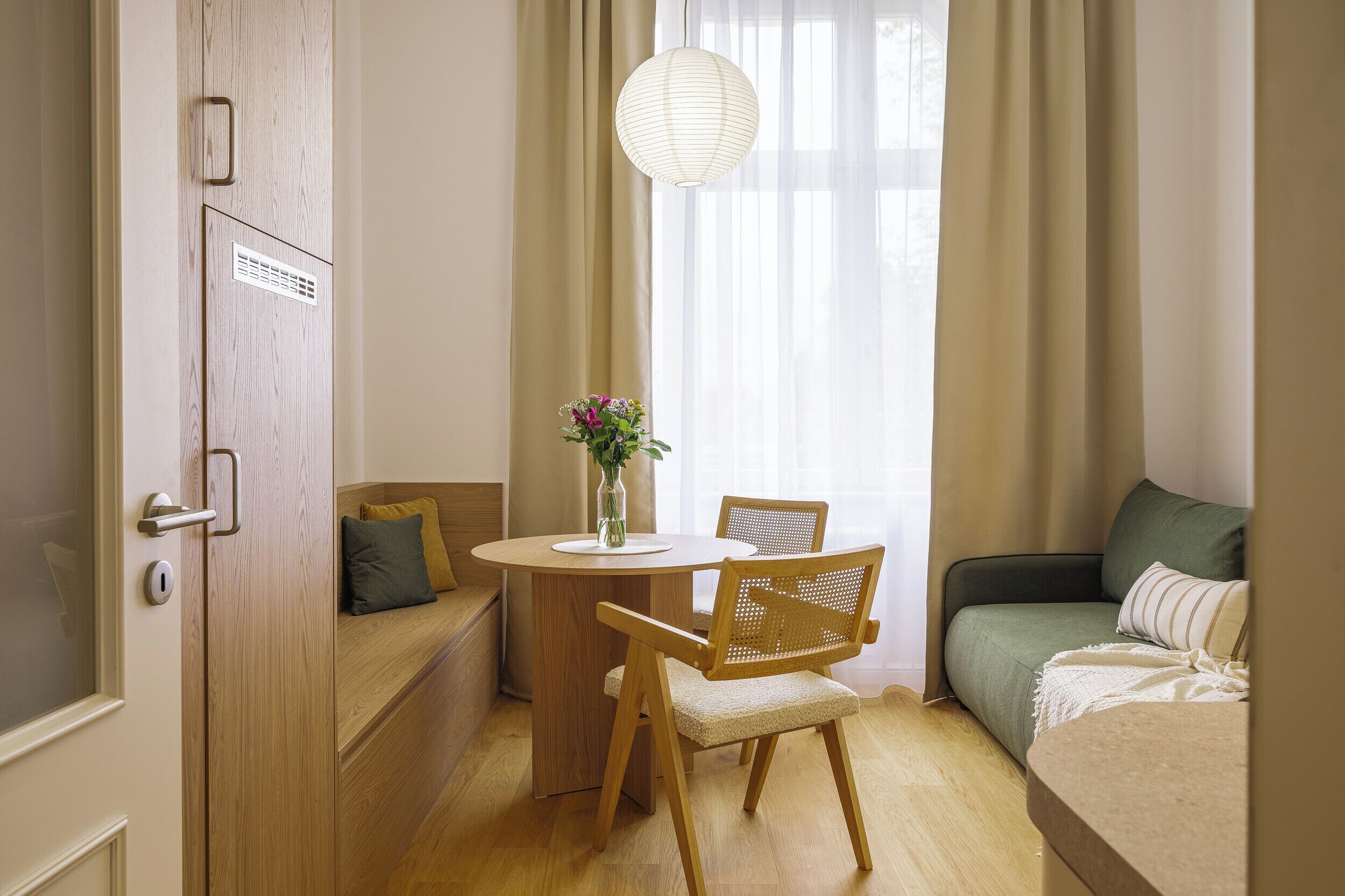 Ein Zimmer mit Holztür, einem runden Tisch mit Stühlen, einer Couch und einer hängenden Leuchte.