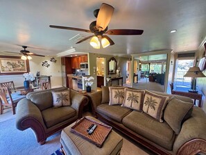 A spacious living room with a large sofa set, a ceiling fan, and a dining area with wooden furniture. - Oceanfront Prop Family Friendly Pool 2BD/2BTH AC (Lahaina)