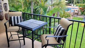 Ein Balkon mit zwei Stühlen und einem Tisch, umgeben von üppiger Vegetation und einem Pool.