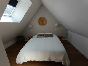 Un dormitorio con techo inclinado, un adorno circular tejido en la pared, dos lámparas de noche, una cama con almohadas estampadas y una ventana.