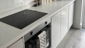 Eine moderne Küche mit weißen Schränken, einer schwarzen Induktionskochplatte, einem eingebauten Backofen und einem Wasserkocher.