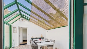 Zona pranzo con tavolo apparecchiato per quattro, una finestra con cornice verde e soffitto in rattan.