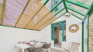 Una camera moderna con soffitto in vetro, un tavolo da pranzo con sedie, una sedia in vimini, un tavolino con una pianta e vista sull'esterno.