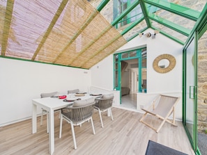 A modern room with a glass ceiling, a dining table with chairs, a wicker chair, a small table with a plant, and a view of the outside. - 650 m from the beach, charming house for 4 people (Dinard)