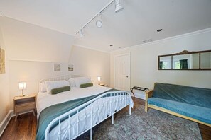 Ein Schlafzimmer mit Bett, Nachttischen, einer Couch, einem gemusterten Teppich und einem Spiegel an der Wand.