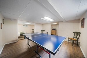 Una mesa de ping pong en una habitación con piso de madera, paredes blancas e iluminación fluorescente en el techo.