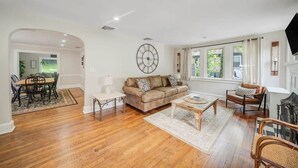 A spacious living room with hardwood flooring, a beige sofa, a coffee table, and a dining area with a table and chairs. - Huntington Village House 4BR – Walk to everything (Huntington)