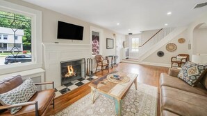 A living room with a fireplace, a television mounted on the wall, and a staircase leading to another level. - Huntington Village House 4BR – Walk to everything (Huntington)