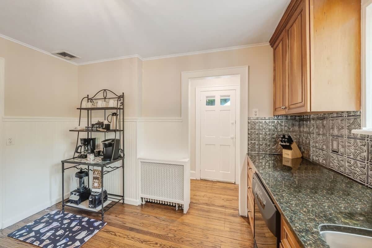A kitchen with a metal rack, a white door, and patterned backsplash.