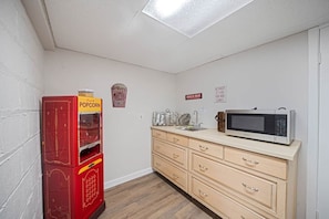 Une petite cuisine équipée d’un four à micro-ondes, un distributeur automatique de pop-corn rouge et une enseigne indiquant la présence d’un bar à collations.