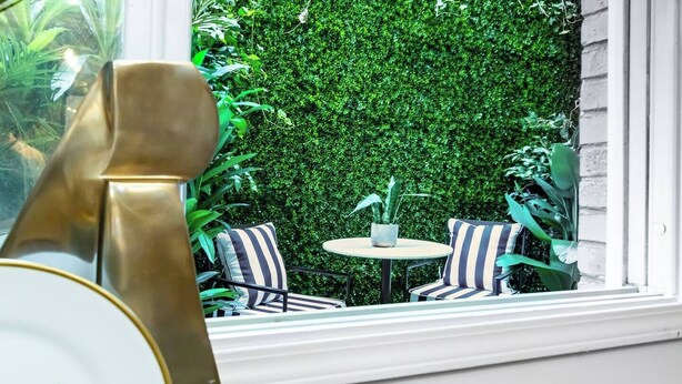 A patio with a round table and striped chairs, a decorative metal sculpture, and a lush green hedge wall. - World Cup | .4 Mi to Ponce | 3 Mi to Mercedes Benz (Atlanta)