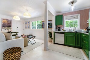 Eine moderne Küche mit grünen Schränken, ein Essbereich mit einer Couch und einem Tisch sowie ein Wohnzimmer mit einer Couch und Dekorationselementen.