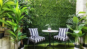 A patio with two striped chairs, a small round table, and a lush green hedge in the background. - World Cup | .4 Mi to Ponce | 3 Mi to Mercedes Benz (Atlanta)