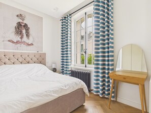 Ein Schlafzimmer mit einem Bett, einem Heizkörper, einem Fenster mit Vorhängen und einem Spiegel.