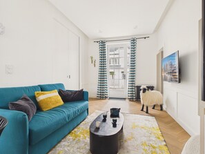 Ein Wohnzimmer mit einem türkisfarbenen Sofa, einem Couchtisch und einer Schafdeko im Hintergrund.