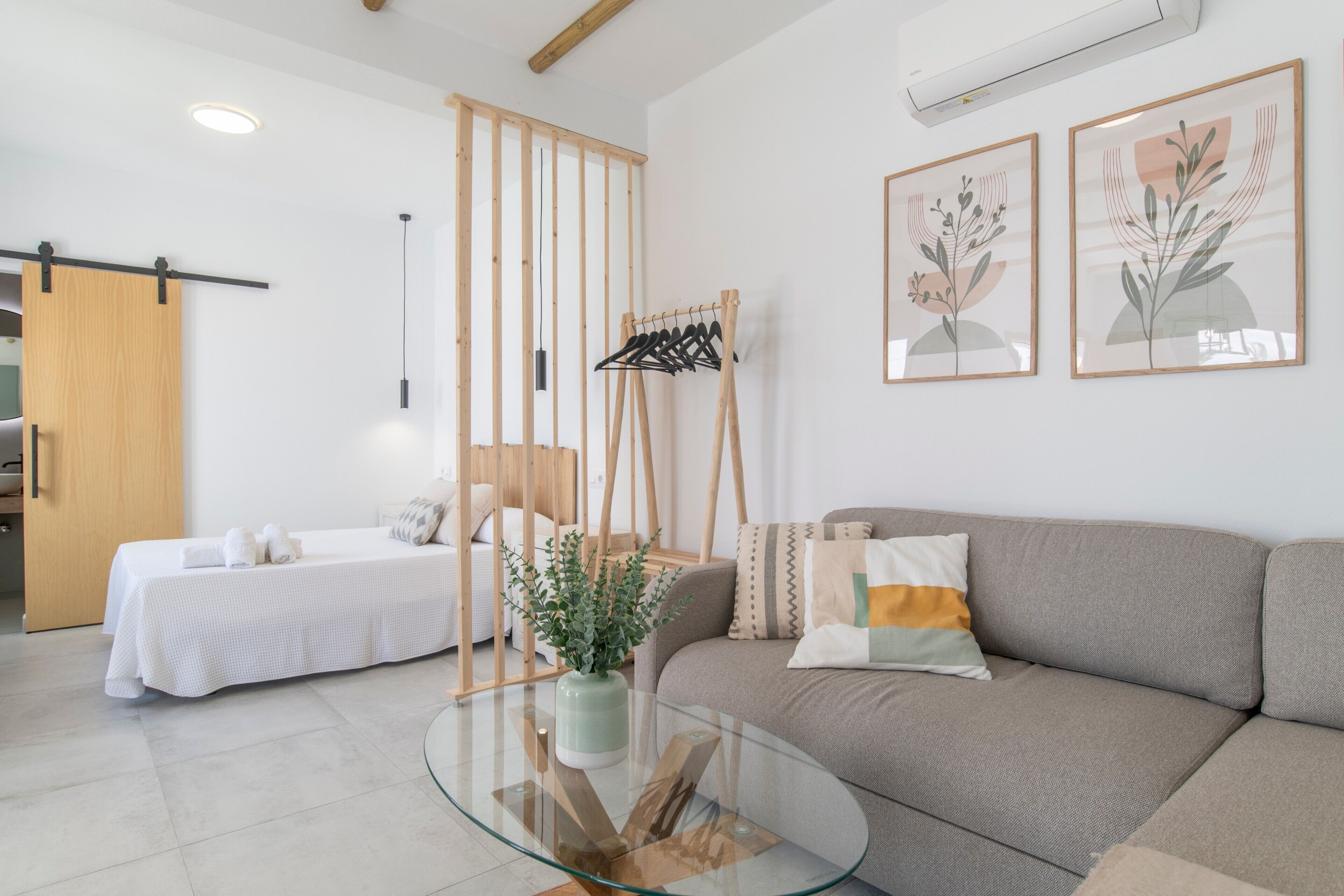 A modern room with a glass coffee table, a sofa, a bed, and a wooden wardrobe.