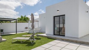 Un pati exterior modern amb un edifici blanc, una zona d'estar coberta i un jardí amb gespa.