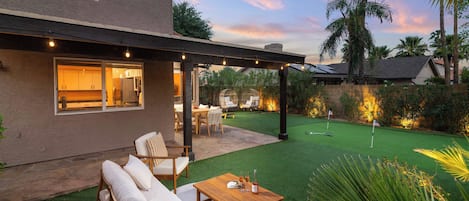 A residential outdoor area with a patio, seating, and a well-maintained lawn.