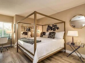 Ein Schlafzimmer mit einem Himmelbett, einem Schreibtisch mit Stuhl, einem runden Spiegel und einer Wandleuchte.