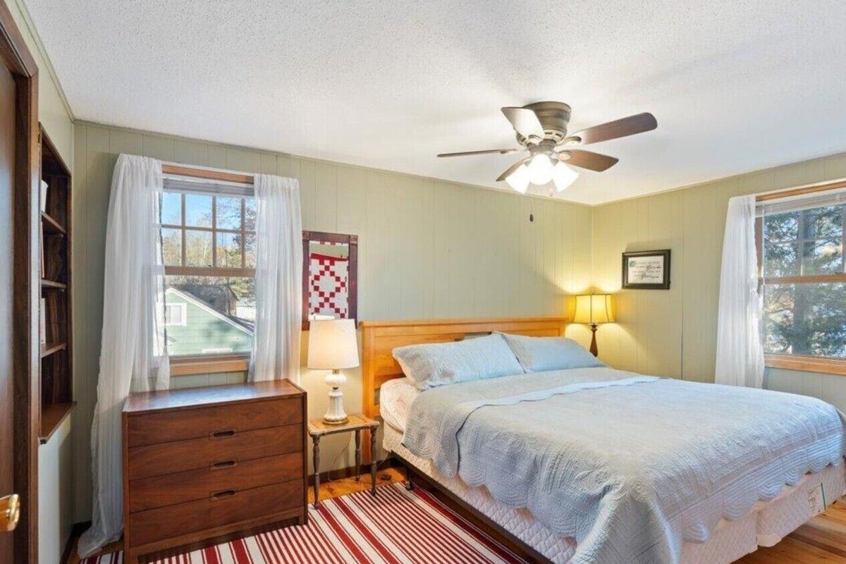 A bedroom with a bed, a nightstand, a dresser, a ceiling fan, and a window with curtains.