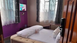 A bedroom with a bed, a nightstand, a TV, and a window with curtains.