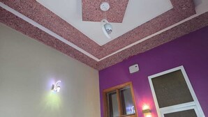 A room with a purple wall, a wooden door, a ceiling fan, and a light fixture.