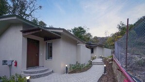 A modern building with a hexagonal tile pathway, a wooden door, and a fenced area with a red fire hydrant. - Vanasya Retreat Corbett (Ramnagar)