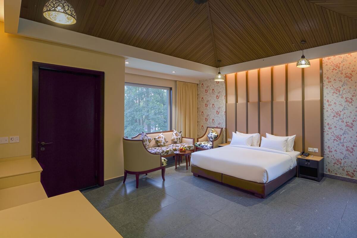 A hotel room with a bed, a sofa, a desk, and a window with a view of trees.