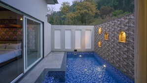 A modern outdoor pool area with a glass door entrance, a small pool with blue mosaic tiles, and a brick wall with built-in lighting. - Vanasya Retreat Corbett (Ramnagar)
