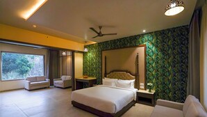 A modern hotel room with a large bed, a sitting area with a sofa, a small table, and a large window. - Vanasya Retreat Corbett (Ramnagar)