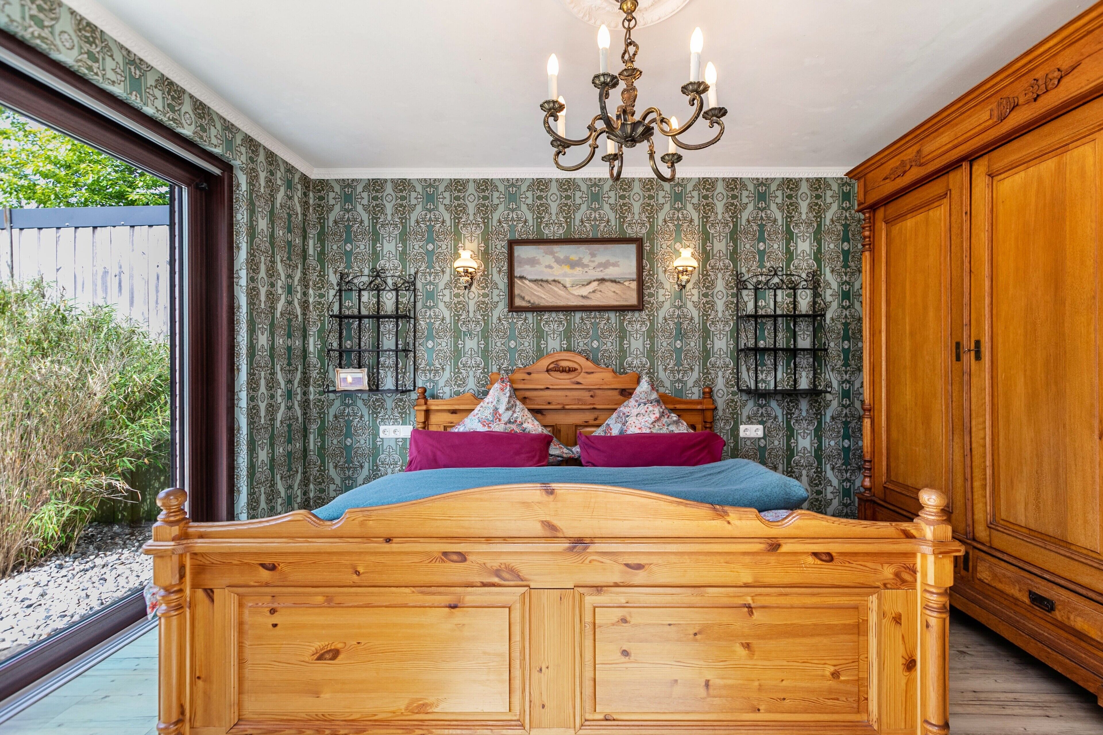 Un dormitorio con cama de madera, candelabro, papel tapiz estampado y un armario grande.