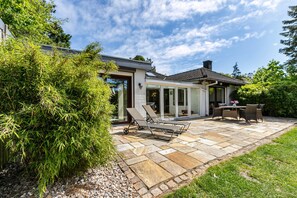 Une terrasse avec un sol en pierre, une porte vitrée donnant sur un espace abrité, et un coin salon composé de chaises et d’une table.