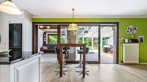 Une cuisine moderne avec un coin repas, un plancher en bois et une vue dégagée grâce à des portes vitrées.