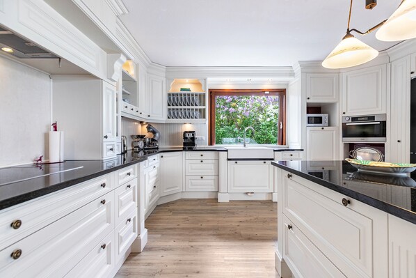 Une cuisine avec des meubles blancs, un plan de travail noir et une fenêtre donnant sur un espace verdoyant.