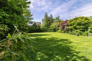 Une zone verdoyante bien entretenue, avec des arbres et une maison en arrière-plan.