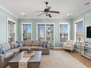 A living room with a sectional sofa, a coffee table, a ceiling fan, and a TV on a wooden stand. - Lazy Salty Beach | 500ft to Beach + Private Pool, Gulf Views (Panama City Beach)