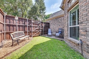 A backyard with a wooden fence, a bench, and a grill area.
