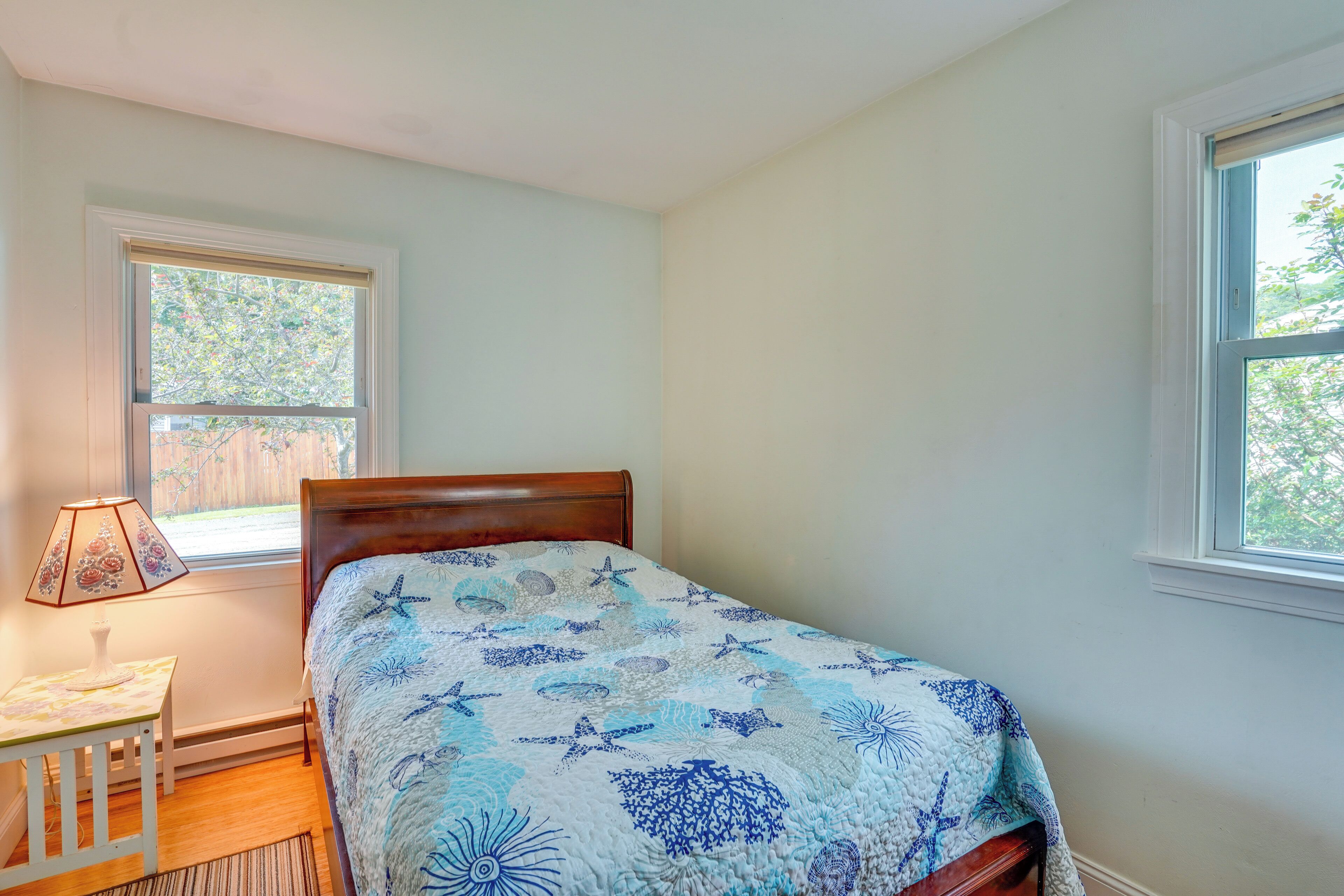 A bedroom with a bed, a nightstand, a lamp, and two windows.