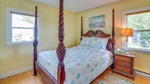 A four-poster bed with a wooden headboard, a bedside table with drawers, and a window with a view of the outside. - Lovely 'the Buoys Cottage' on Annisquam River! (Gloucester)
