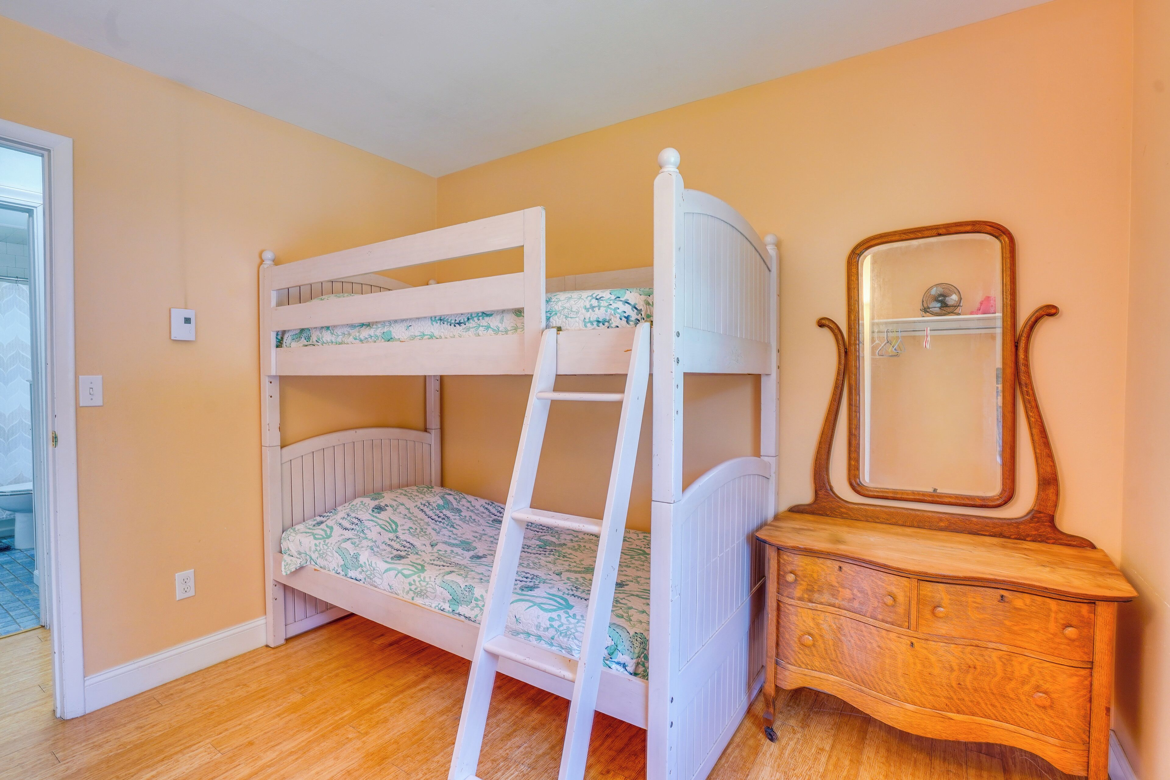 A bunk bed with a ladder, a dresser with a mirror, and a door leading to a bathroom.
