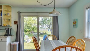A dining area with a table, chairs, a trash can, and a view of the outdoors. - Lovely 'the Buoys Cottage' on Annisquam River! (Gloucester)