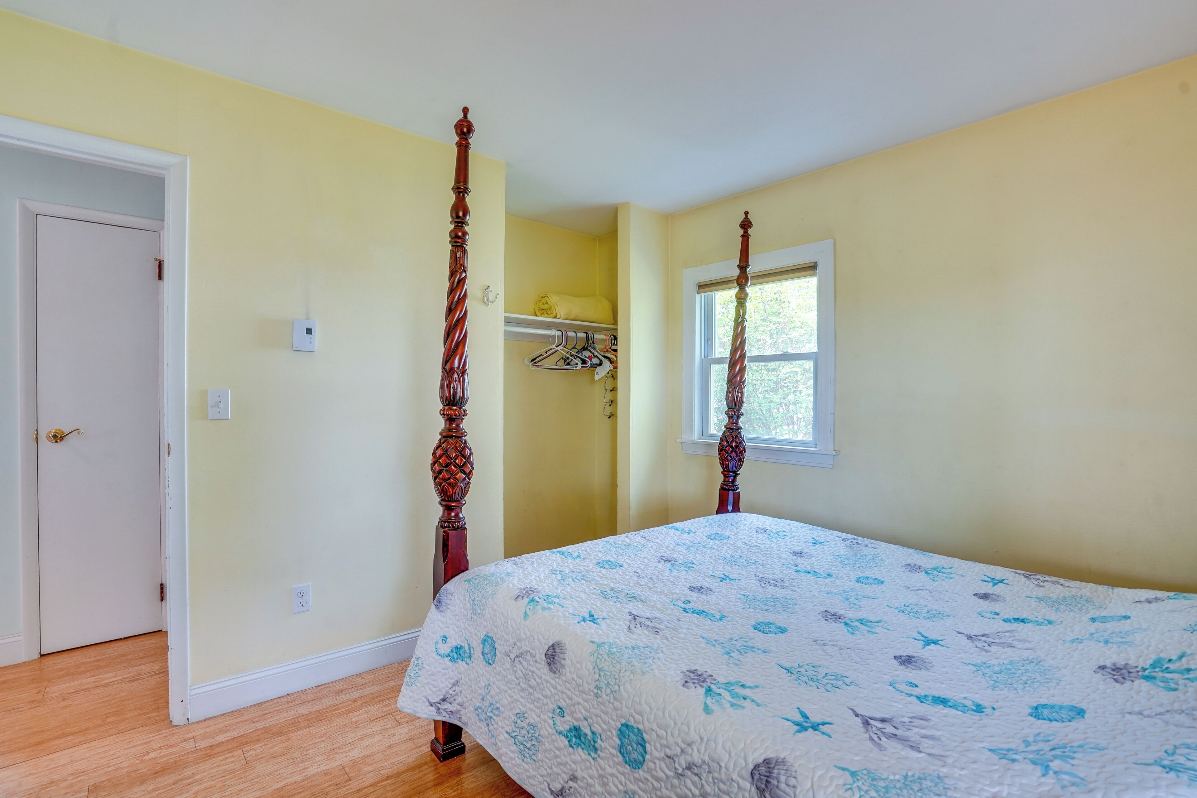 A bedroom with a four-poster bed, a window, and a closet with hanging clothes.