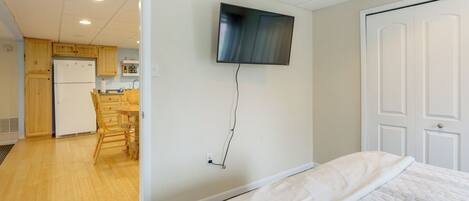 Hotelkamer met een bed, een aan de muur bevestigde televisie, een keukenruimte zichtbaar door een geopende deur, en een witte deur.
